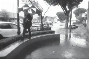  ?? KENT NISHIMURA/LOS ANGELES TIMES ?? A woman walks on a bench to avoid water pouring on the sidewalk from a rain gutter in Burbank on Saturday.