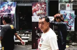  ??  ?? People walk past movie posters at the downtown area of Yangon.