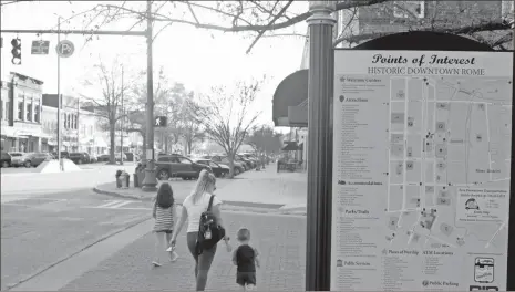  ?? John Bailey ?? With packed parking spaces visible down Broad Street, a mother and her children walk past a sign showing points of interest in the Historic Downtown area.