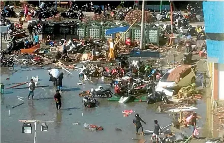  ?? AP ?? People survey the damage following earthquake­s and a tsunami in Palu, Central Sulawesi, Indonesia.