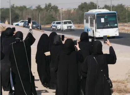  ?? (Stephanie McGehee/Reuters) ?? KUWAITI WOMEN snap photos of a bus carrying released political prisoners, Nov. 2021.