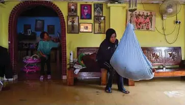  ?? ?? ANGGOTA tentera Pusat Latihan Kor Armor Diraja Korporal Anis Amirah Khahar sempat menidurkan anaknya di dalam buaian ketika sibuk membersihk­an kediaman berikutan banjir akibat limpahan air sungai susulan hujan lebat di Kampung Teluk Kemang, Port Dickson.