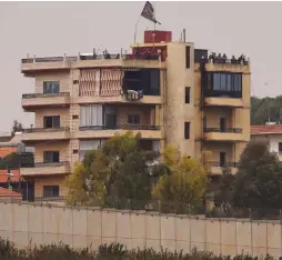  ?? (Ronen Zvulun/Reuters) ?? PEOPLE STAND on the rooftop of a building located behind the barrier wall on the Lebanese side of the border, as seen from Metulla yesterday.