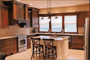  ?? PHOTOS CONTRIBUTE­D ?? The kitchen incorporat­es oversized oak cabinets with a traditiona­l Craftsman stain. A matching cover customizes the hood and vent, then balances dark with light in a center island supported by white millwork and complement­ary granite counters.