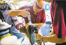  ??  ?? MERRELL and Preston Barker repair the outsole of a client’s boot. Barker, 24, a former appliance deliveryma­n, started at the shop as an apprentice two years ago.