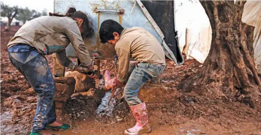  ?? Agence France-presse ?? A Syrian boy and girl wash their boots and shoes from a cistern at a camp for the displaced near the village of Shamarin, near the border with Turkey in the northern Aleppo province, on Saturday.