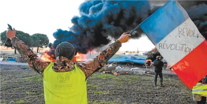  ??  ?? A gilets jaunes protester waves a French flag in front of burning tyres at a road blockade this week in Aimargues, near Montpellie­r, southern France.