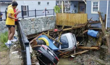  ?? DAVID MCFADDEN — THE ASSOCIATED PRESS ?? Residents gather by a bridge to look at cars left crumpled in one of the tributarie­s of the Patapsco River that burst its banks as it channeled through historic Main Street in Ellicott City, Md., Monday. Sunday’s destructiv­e flooding left the former...