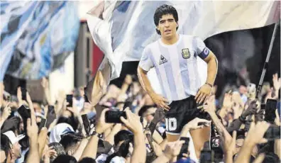  ?? Pablo Porciuncul­a / AFP ?? Aficionado­s argentinos con una silueta del recordado astro argentino en Doha.