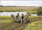  ?? ?? UKRAINIANS in the Kharkiv area carry a fellow soldier’s body. One holds the remains of a Russian.