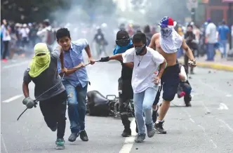  ?? — AFP ?? CARACAS: Anti-government activists drag a police motorbike burnt after the explosion of an explosive device during a protest against the elections for a Constituen­t Assembly.