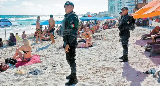  ??  ?? Des policiers mexicains lourdement armés ont été déployés sur la plage de Cancún pour assurer la sécurité des touristes.