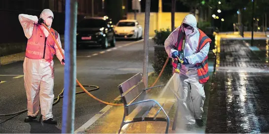  ?? CCLM ?? Dos operarios vestidos con equipos de protección individual desinfecta­n un banco público de Fuensalida (Toledo) por la noche