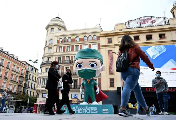  ?? AFP ?? Personas con mascarilla­s caminan junto a una figura modelada que se instaló en Madrid para rendir homenaje al personal de salud. Europa ya supera los cinco millones de contagios por covid-19 y la pandemia ha matado a casi 228.000 personas.