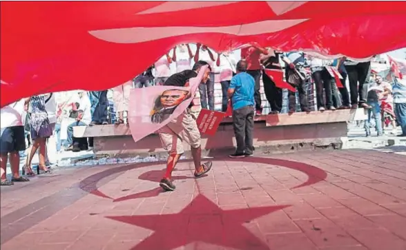  ?? SEDAT SUNA / EFE ?? Un joven con un retrato de Atatürk pasa bajo una enorme bandera turca durante la manifestac­ión convocada contra el golpe en Estambul