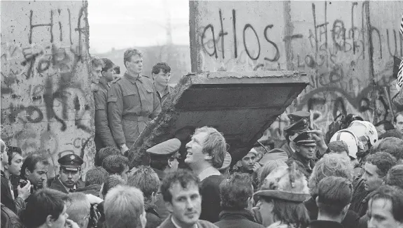  ?? GERARD MALIE/AFP/GETTY IMAGES ?? West Berliners crowd in front of the Berlin Wall early on Nov. 11, 1989, as they watch East German border guards demolishin­g a section of the Wall to open a new crossing point between East and West Berlin. The wall was built by the East German Communist government in 1961.