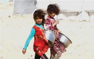  ??  ?? Girls carry containers for food rations on Tuesday at a refugee camp in Ain Issa, Syria. (Reuters)