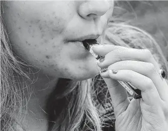  ?? Steven Senne / Associated Press ?? A high school student uses a vaping device near a school campus in Cambridge, Mass. Besides nicotine, the devices contain chemicals for flavoring that aren’t meant to be inhaled.