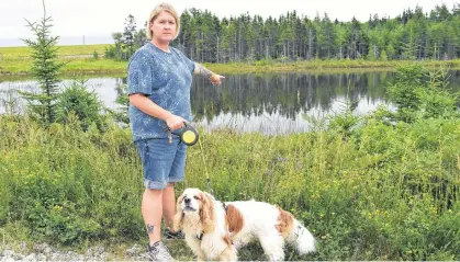  ?? SHARON MONTGOMERY-DUPE • CAPE BRETON POST ?? Jennifer Lemoine of New Waterford, with her dog Winston, points to the location where a live beaver trap was recently left on the bank of the pond along the Summit Recreation­al Trail in Scotchtown which almost killed her dog. Lemoine said the beavers were a huge part of the enjoyment of the trail but were killed off with approval by Nova Scotia Lands and Forestry due to a flooding issue rather than relocated.