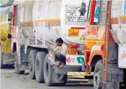  ?? — Reuters ?? A driver reads a newspaper as he sits on a spare tire attached to a parked oil tanker at a truck terminal in Mumbai.