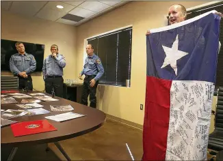  ?? RALPH BARRERA / AMERICAN-STATESMAN ?? Austin firefighte­rs look on as Battalion Chief Randy Denzer (right) holds a Texas flag that was signed by the 94 firefighte­rs from Texas who served in California and many others helpful in their success. The flag was flown from the back of Austin firefighte­rs’ truck and later flew over the Capitol.