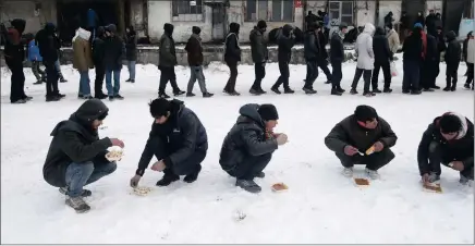  ?? PICTURE: AP ?? Five migrants squat in the snow as they eat a warm meal distribute­d by aid groups as others queue for their portion outside a crumbling warehouse that has served as a makeshift shelter in Belgrade, Serbia, on Thursday. .