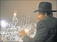  ??  ?? Modern Maccabees: A rabbi lights a candle on a menorah made of ice in Central Park, commemorat­ing Jewish defiance against Hellenizat­ion.