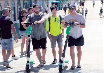  ?? Mel Melcon Los Angeles Times ?? STEPHEN LEE, center, a Lime scooter operations manager, watches riders return the devices after losing power near the pier in Santa Monica, where geofencing technology is used to remotely enforce dead zones.