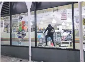  ?? FOTO: AP ?? Ein Plünderer trägt Waren aus einem 7-Eleven-Supermarkt in New York.