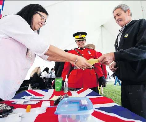  ?? BRANDON HARDER ?? Dwayne Kline, a member of Cowessess First Nation who resides in Regina, hands a slip indicating his eligibilit­y for the $5 treaty annuity payment to Geraldine Linton, a governance officer for Indigenous Services Canada as RCMP Inspector Honey Dwyer looks on.