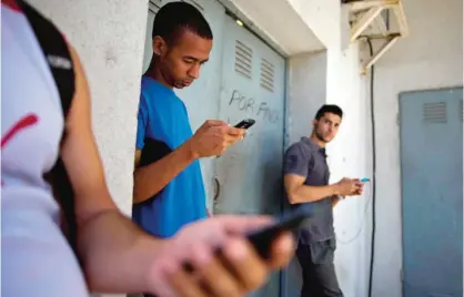  ?? — AP ?? CUBA: In this April 1, 2014 file photo, students gather behind a business looking for an Internet signal for their smart phones in Havana, Cuba.