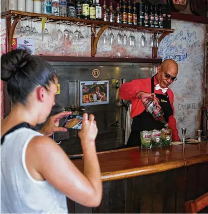  ??  ?? Eduardo Corona prepares drinks as tourists take photos of him at El Traguito, a bar in Santiago de Cuba. Havana, and its best bar may be the one located in the basement of a sparse museum.
