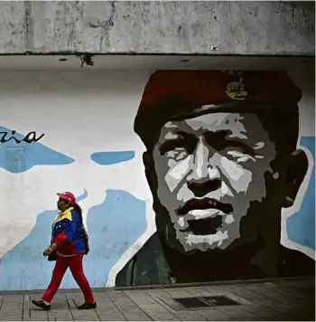  ?? Yuri Cortez - 6.dez.18/AFP ?? Apoiadora do chavismo passa em frente a muro com pintura de Chávez em Caracas