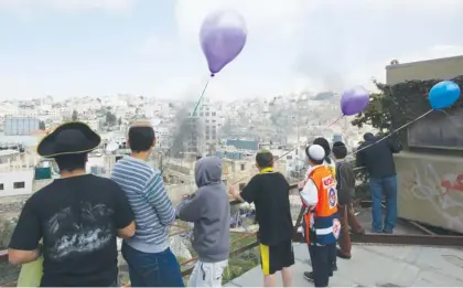  ?? (Ronen Zvulun/Reuters) ?? JEWISH CHILDREN, some dressed in costumes to celebrate Purim, watch as smoke rises from violence between Arabs and soldiers in Hebron yesterday.