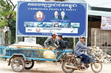  ?? — AFP photo ?? Commuters pass by the billboard of the ruling Cambodian People’s Party bearing the portraits of Hun Sen (right) and Samrin (left) in Kandal province.