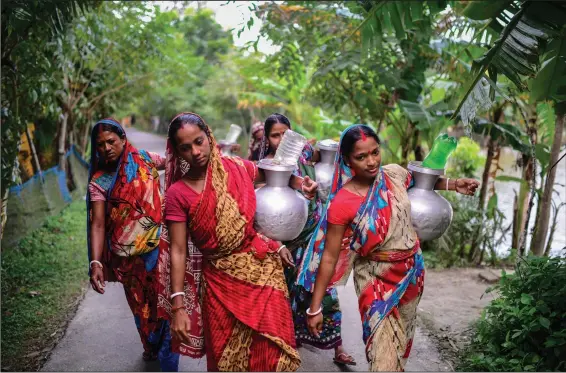  ?? (AP/Mahmud Hossain Opu) ?? Women walk toward their homes carrying drinking water Oct. 5 in Bonbibi Tala in Satkhira, Bangladesh.