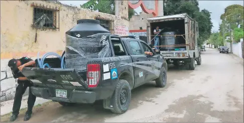  ??  ?? El municipio de Tinum se ve obligado a recurrir a distintos medios para proveer agua a los pobladores: en la imagen, policías hacen la distribuci­ón con depósitos en las patrullas