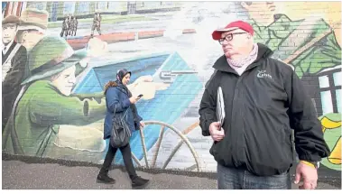  ?? — AFP ?? Historical background: Whelan standing in front of a mural as he guides a tourist during in west Belfast.