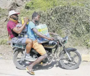  ??  ?? This businessma­n is helped with goods for his establishm­ent by a motorcycli­st on Gordon Town Road in St Andrew.