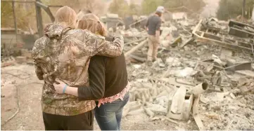  ??  ?? Kimberly Spainhower hugs her daughter Chloe, 13, while her husband Ryan Spainhower (right) searches through the ashes of their burned home in Paradise. — AFP photo