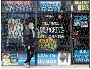  ?? (AP) ?? A man passes a closed store in Chicago in April. The Federal Reserve for the first time is directly supporting America’s so-called Main Street firms.