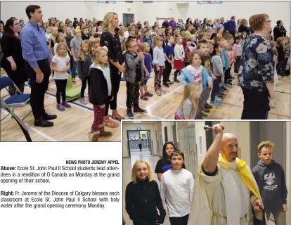  ?? NEWS PHOTO JEREMY APPEL ?? Ecole St. John Paul II School students lead attendees in a rendition of O Canada on Monday at the grand opening of their school.Fr. Jerome of the Diocese of Calgary blesses each classroom at Ecole St. John Paul II School with holy water after the grand opening ceremony Monday.