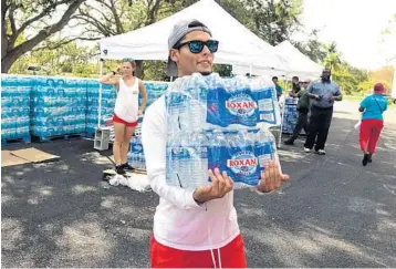  ?? JOE CAVARETTA/STAFF WRITER ?? Volunteer Mauricio Bohorquez carries water to a car at Quiet Waters Park in Deerfield Beach.