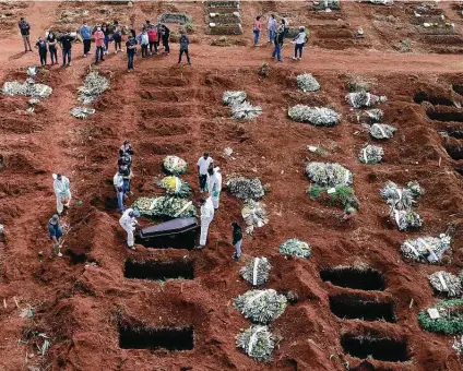  ?? Andre Penner / Associated Press ?? Cemetery workers wearing protective gear lower the coffin of a person who died from COVID-19 into a gravesite in São Paulo, Brazil.