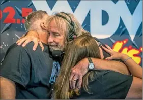  ?? Alexandra Wimley/ Post- Gazette ?? Radio DJ Sean McDowell, center, hugs longtime friends Shawn and Leslie Duncan, of Dormont, after his final broadcast before retiring Wednesday at the Pittsburgh Marriott City Center, Downtown. Visit post- gazette. com for a video report.