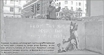  ?? — Reuters photo ?? A passer-by takes a photograph next to a graffiti believed to have been created by street artist Banksy, at the site where hundreds of Extinction Rebellion climate protesters camped recently, at Marble Arch in London.