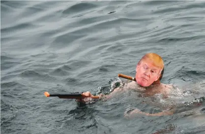  ?? —AFP ?? GENEVA: A man wearing a mask of US elected President Donald Trump and a toy gun swims in the lake during the 78th “Coupe de Noel” (Christmas cup) swimming race in the Lake Geneva yesterday.