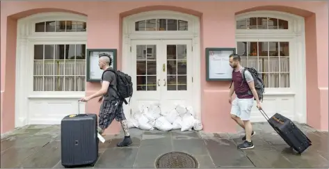  ?? AP photo ?? Sandbags block the door of the famous Brennan’s restaurant in the New Orleans French Quarter Friday as tourists hurry by with their luggage and bands of rain from Tropical Storm Barry move into the city.