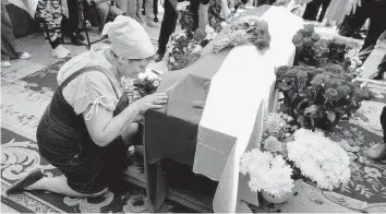  ?? NATACHA PISARENKO AP ?? A woman kneels at activist and soldier Roman Ratushnyi’s coffin during his memorial service in Kyiv, Ukraine, in June 2022.