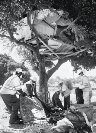  ?? Paul Chinn / The Chronicle ?? CLEANUP EFFORT: A Department of Public Works crew removes discarded belongings and debris from beneath a tree house built in a homeless encampment on East 12th Street.